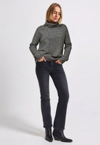 Grauer, gestrickter Rollkragenpullover in lässiger Passform, kombiniert mit schwarzer Jeans und spitzen schwarzen Stiefeletten. Glatte Textur, legeres Design und dezente Muster.
