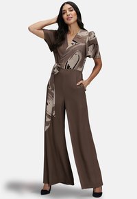Brown jumpsuit with a wrap design, short sleeves, and a patterned waist tie. Features wide-leg pant style and side pockets.