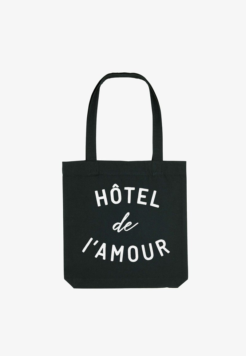Zwarte katoenen totebag met twee stevige handvaten. Heeft witte tekst die "HÔTEL de l'amour" in verschillende lettergroottes over de voorkant weergeeft.