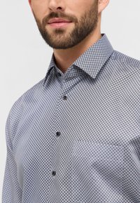 Camicia da uomo con motivo geometrico nei colori blu navy, grigio e bianco. Dotata di un colletto classico e bottoni neri, realizzata in tessuto morbido.