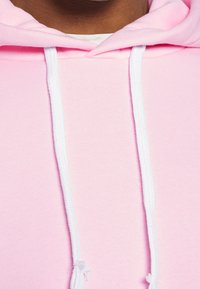 Närbild av en person som bär en ljusrosa huvtröja med vita snören och en vit skjorta under.