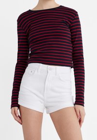 Meren pitkähihainen paita, jossa on punaiset raidat, yhdistetty valkoisiin farkkushortseihin. Paidassa on pyöreä kaula-aukko ja istuva malli.