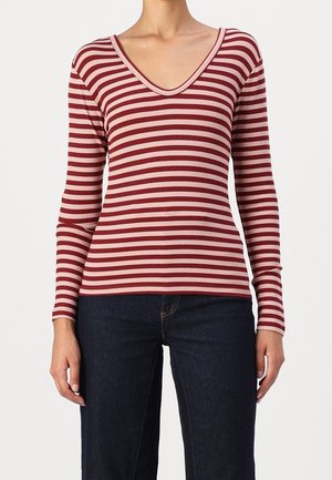 Punainen ja vaaleanpunainen raidallinen pitkähiha, jossa on V-pääntie, ribbikuvio ja tiukka malli, yhdistettynä tummiin farkkuihin.