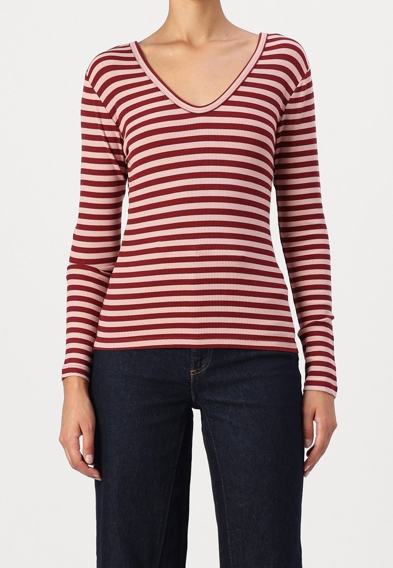 Punainen ja vaaleanpunainen raidallinen pitkähiha, jossa on V-pääntie, ribbikuvio ja tiukka malli, yhdistettynä tummiin farkkuihin.