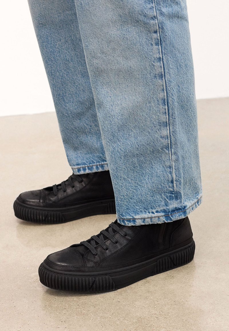 Mustad musta nahast kõrged tossud, millel on tekstureeritud pind ja paks kummitald, kanda helesiniste, lõdvalt istuvate teksadega.