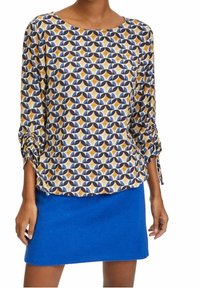 Blusa stampata multicolore con maniche a tre quarti, caratterizzata da un colletto rotondo e polsini arricciati. Abbinata a una mini gonna di feltro blu.