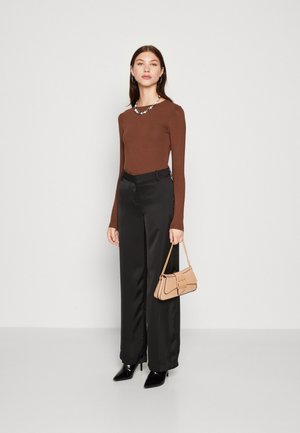 Bruine lange mouw top gecombineerd met zwart satijnen wijde broek. Accessoires zijn een beige handtas met ketting en een bloemenketting. Zwarte hakken.