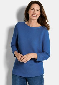 Blauwe, gestructureerde trui met een ronde halslijn en driekwartmouwen, gecombineerd met denim jeans. Kenmerkt zich door een losse pasvorm en gladde stof.