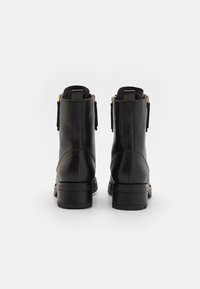 Zwarte leren enkellaarsjes met een gladde afwerking, een ronde neus en een lage blokhak; voorzien van ritsen en decoratieve franjes.