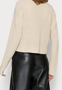 Cremfarbener, gestrickter Pullover mit Cropped-Design, gerippter Textur und langen Ärmeln, kombiniert mit schwarzen Lederhosen.