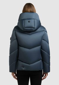 Giacca imbottita blu navy con colletto alto, cuciture a zig zag e dettaglio a bottone sulla cappuccio. Presenta maniche lunghe e un design elegante.