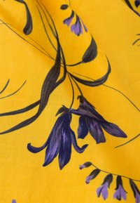 Żółty materiał z kwiecistym wzorem, zawierającym fioletowe kwiaty i czarne łodygi, o gładkiej teksturze i wyrazistym kontraście kolorów.