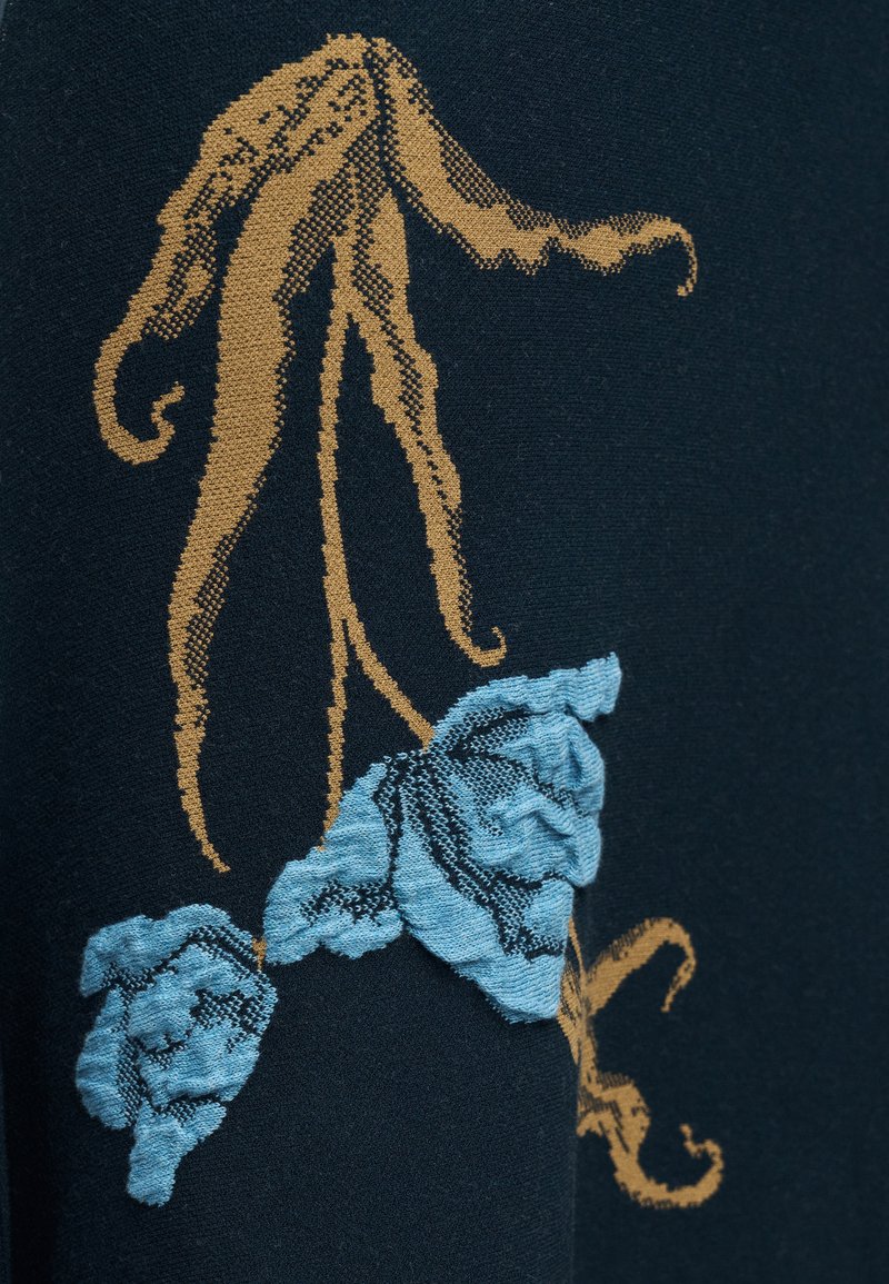 Blauwe stof met bruine wijnstokachtige stengels en geborduurde lichtblauwe bloemen met textuur op een donkere achtergrond.