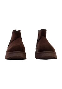 Bottes basses en daim marron avec un bout arrondi, des panneaux latéraux élastiques et une semelle en caoutchouc texturée. Construction solide avec une semelle compensée basse.