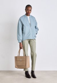 Lyseblå bomberjakke, lett stoff, elastiske mansjetter; olivengrønne bukser; beige tote med "GK"-logo; svarte ankelstøvler.