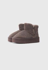 Botas de ante marrón hasta el tobillo con cremalleras laterales y suelas de goma gruesa, forradas con suave piel para el uso invernal.