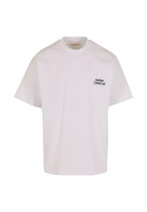 T-shirt bianca in cotone con scollatura rotonda e maniche corte. Presenta un piccolo testo nero sul lato sinistro in alto: "Another Cotton Lab."