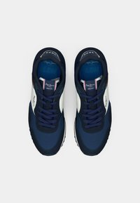 Tênis azul marinho com detalhes brancos. Apresenta um cabedal de tecido suave, painéis texturizados, fechamento com cadarço na frente e palmilhas com marca. Design leve.