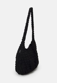 Czarna torba na ramię z tekstyliów, o teksturowanej, pikowanej powierzchni, zaokrąglonym kształcie i długim, skręconym pasku. Brak widocznych elementów metalowych lub akcentów.