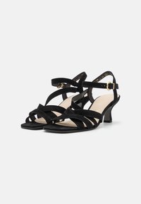 Sandalo nero in suede con punta aperta, caratterizzato da multiple cinghie incrociate, un tacco basso e un dettaglio in oro sulla cinghia alla caviglia.