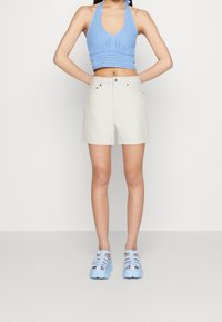 Haut crop halter tricoté bleu clair, shorts beiges et sandales épaisses bleu clair. Design simple avec une silhouette ajustée et des accents minimalistes.