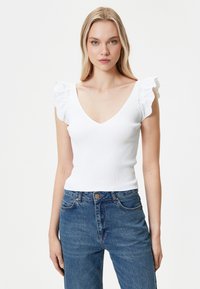 Weißes geripptes oberteil mit tiefem V-Ausschnitt und rüschigen Kurzärmeln, kombiniert mit hochtaillierten blauen Denim-Jeans.
