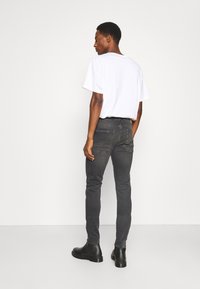 Jean noir à coupe slim, avec des poches arrière et un délavage subtil. Associé à un t-shirt blanc ample et des bottes noires robustes.