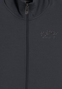 Giacca zip-up grigia scura realizzata in tessuto liscio. Presenta un colletto alto e un logo in strass sulla parte sinistra del petto.