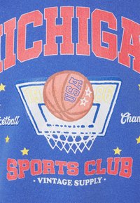 Královská modrá látka s grafikou basketbalového koše, oranžovým basketbalovým míčem a textem v červené a bílé barvě, doplněná žlutými hvězdami.