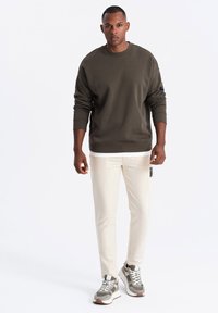 Olijfgroene sweatshirt met geribbelde boorden en zoom, gecombineerd met crèmekleurige slim-fit broeken. Sneakers met grijs en witte accenten.