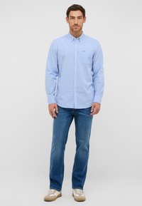 Niebieska i biała koszula w kratkę z guzikami, z kieszenią, w połączeniu z niebieskimi dżinsami i beżowymi trampkami. Koszula ma kołnierzyk i długie rękawy.