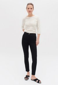 Top a maniche lunghe bianco e beige a righe con collo rotondo, abbinato a jeans skinny neri a vita alta e sandali neri a fascia.