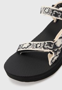 Fekete flip-flop szandál, amely mintás szövet pántokkal rendelkezik fekete, fehér és szürke színben. A talpa texturált gumiból készült, kiemelkedő tapadásmintával.