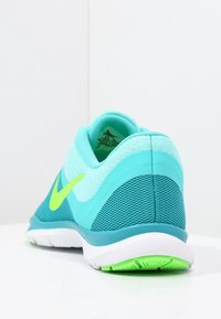 Turkis atletisk sko med mesh- og syntetisk overdel, synlig logo, polstret krave og hvid sål med grønne accenter. Glat tekstur.