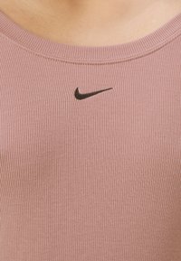 Rózsaszín bordázott ujjatlan felső kerek nyakkivágással és egy kis fekete Nike logóval a mellrészen. Puha anyagú, testhez simuló fazon.