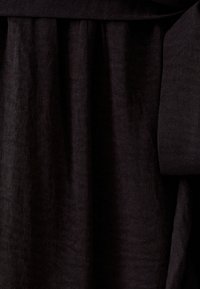 Un tissu noir présente une texture douce avec un léger brillant, mettant en valeur des éléments de drapés et de plis. Lisse et léger.
