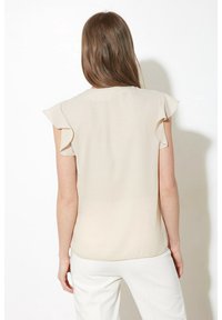 Beige Bluse mit kurzen, rüschengeschnittenen Ärmeln und rundem Ausschnitt. Glattes Material; der Rücken weist ein einfaches, klares Design ohne Verzierungen auf.