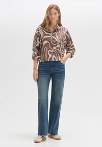 Brown and cream patterned button-up shirt with a relaxed fit, paired with blue high-waisted jeans and gray sneakers on a plain background.