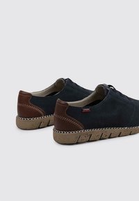 Zapatos de ante azul oscuro con detalles en cuero marrón, diseño perforado y suela de goma texturizada. Presenta costuras y cordones en contraste.
