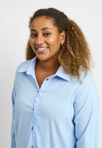 Light blue button-up shirt made of smooth fabric, featuring a collar and long sleeves. The shirt has visible buttons and a relaxed fit.