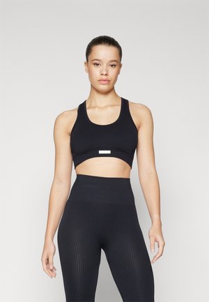 Crni sportski cropped top s širokim trakama i izrezom u sredini, uparen s visokim crnim tajicama od rebraste tkanine. Glatka tekstura tkanine.