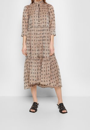 Vestido floral beige con un cuello alto, mangas largas, cierre de botones y falda fruncida. Combinado con sandalias negras de tiras.