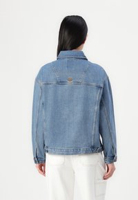 Veste en denim bleu clair, avec un col classique, des boutons de fermeture et une étiquette logo au dos. Conçue avec une coupe décontractée et des poches latérales.