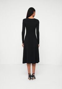 Čierna dlhá sukňa s dlhým rukávom, so priliehavým telom a rozšírenou sukňou, vyrobená z jemného materiálu. Má okrúhly výstrih a končí pod kolenami.