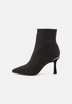 Botín negro hasta el tobillo con punta afilada, parte superior de tela texturizada y tacón delgado. Presenta un puño ajustado en el tobillo y un discreto acento metálico.