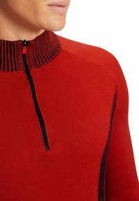 Pull rouge avec un col zippé, doté d'un tissu texturé et d'une bande noire contrastante le long du col et du zip.