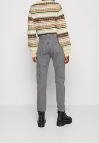 Jeans de mezclilla gris con un ajuste relajado, que cuentan con bolsillos traseros y detalles de costura sutil, combinados con un suéter de punto a rayas multicolores.