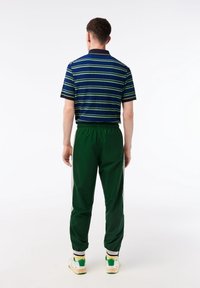 Camiseta tipo polo de manga corta en azul marino con rayas verdes, combinada con pantalones verdes ajustados con paneles laterales de malla y cintura elástica.
