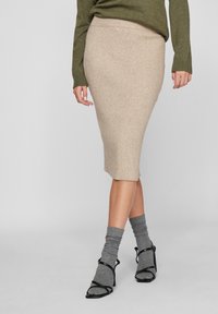 Beige ribbad knit midi kjol med en figurnära silhuett. I kombination med grå slappa strumpor och svarta remsandaler med hög klack.