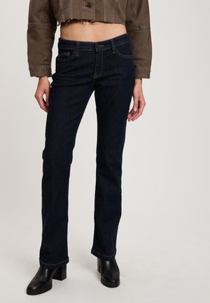 Dark blue denim flared jeans with a mid-rise waist, front pockets, and stitching details. Worn with black heeled ankle boots.